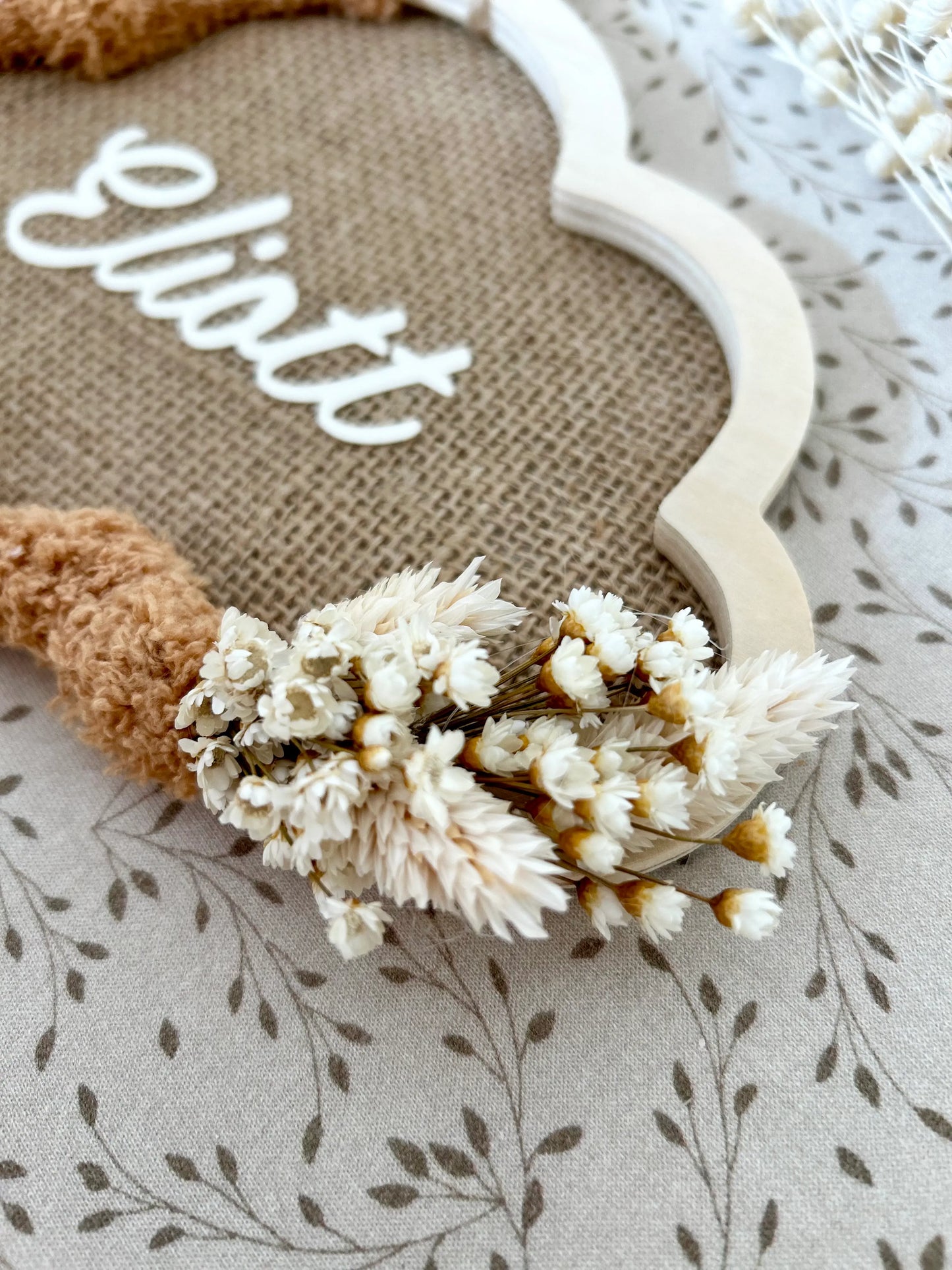 Détail du prénom en vinyle appliqué sur la toile de jute, entouré de fleurs séchées et de la laine miel pour une touche bohème et intemporelle.