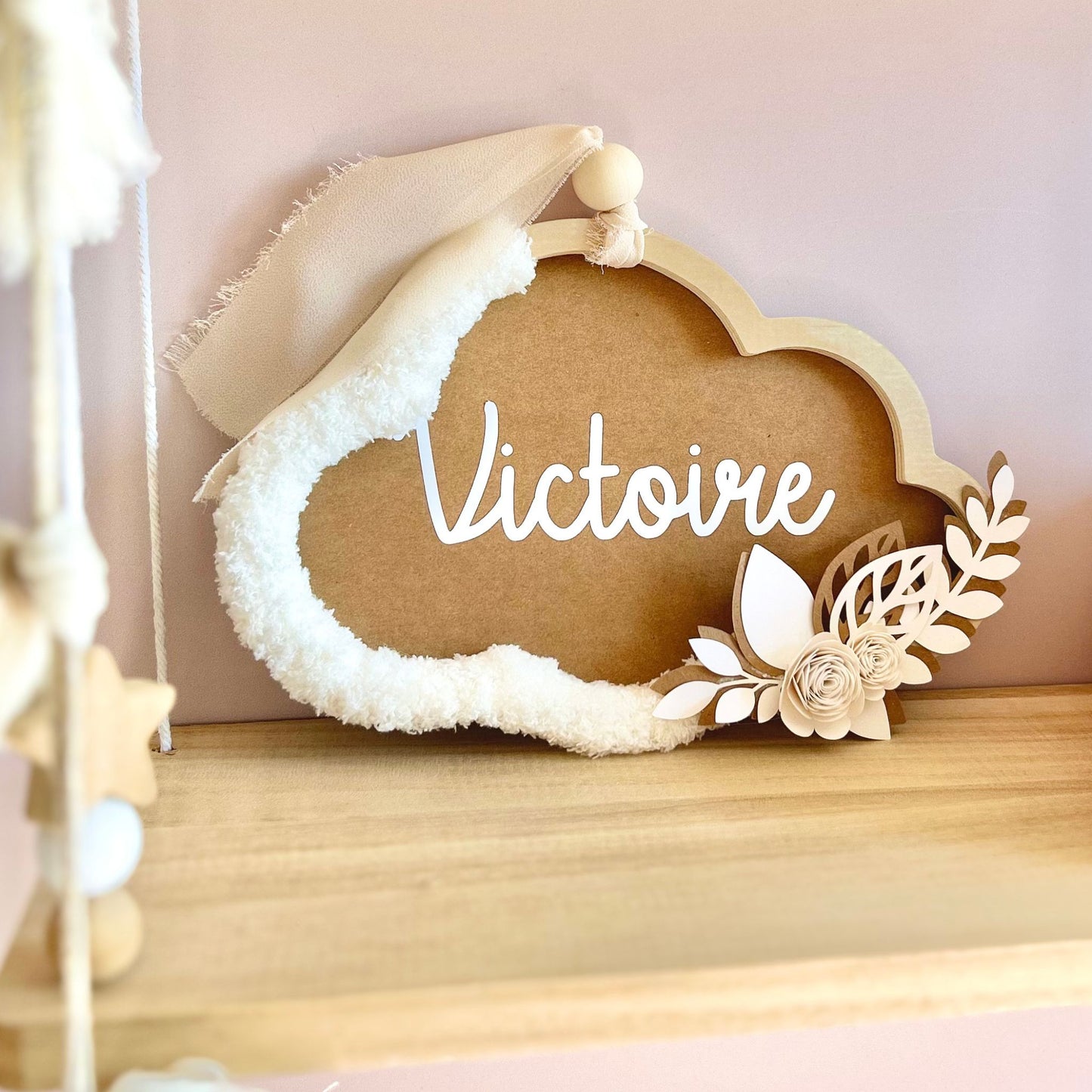 Nuage prénom personnalisé pour bébé fille, décoration murale artisanale marron cannelle à suspendre ou à poser sur commode, avec guirlande pompons et mur rose pâle.