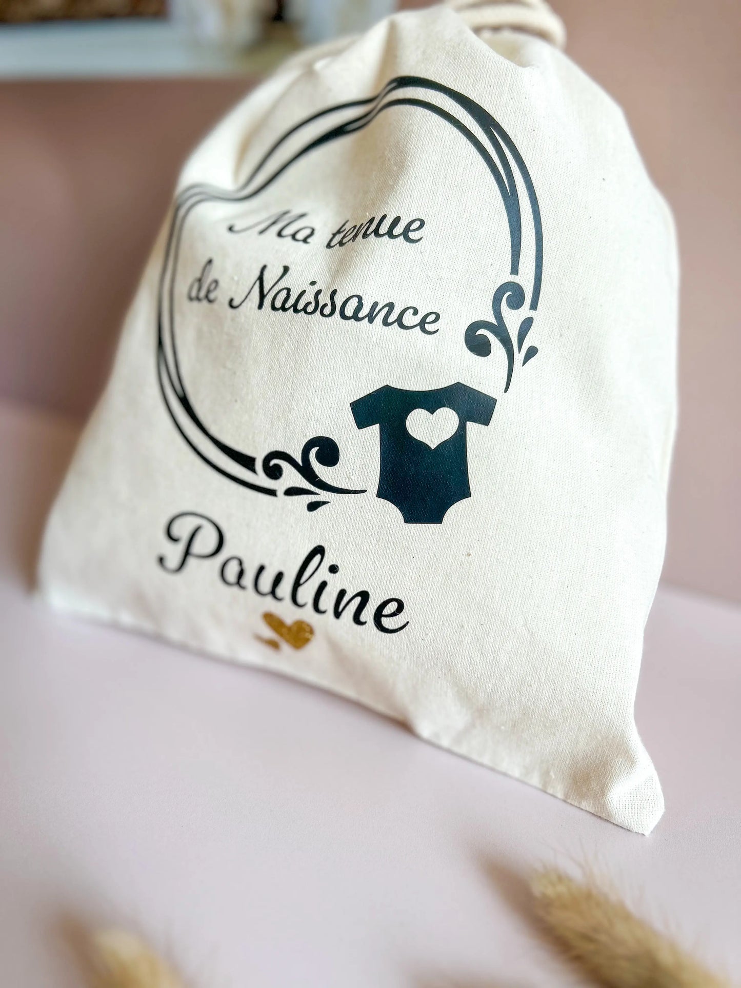 Vue de face d’un pochon de naissance floqué avec le prénom de l’enfant, à glisser dans la valise maternité.