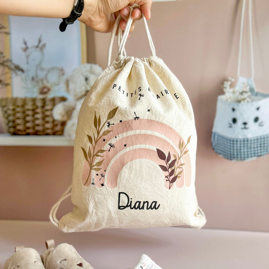 Sac à dos crèche personnalisé avec le prénom de bébé, en coton bio beige, suspendu dans une chambre d'enfant.