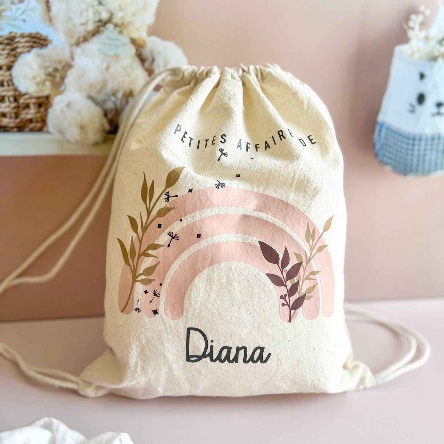 Vue de face du sac à cordelettes personnalisé au prénom de bébé, coloris naturel beige et motif arc-en-ciel rose pastel et doux.