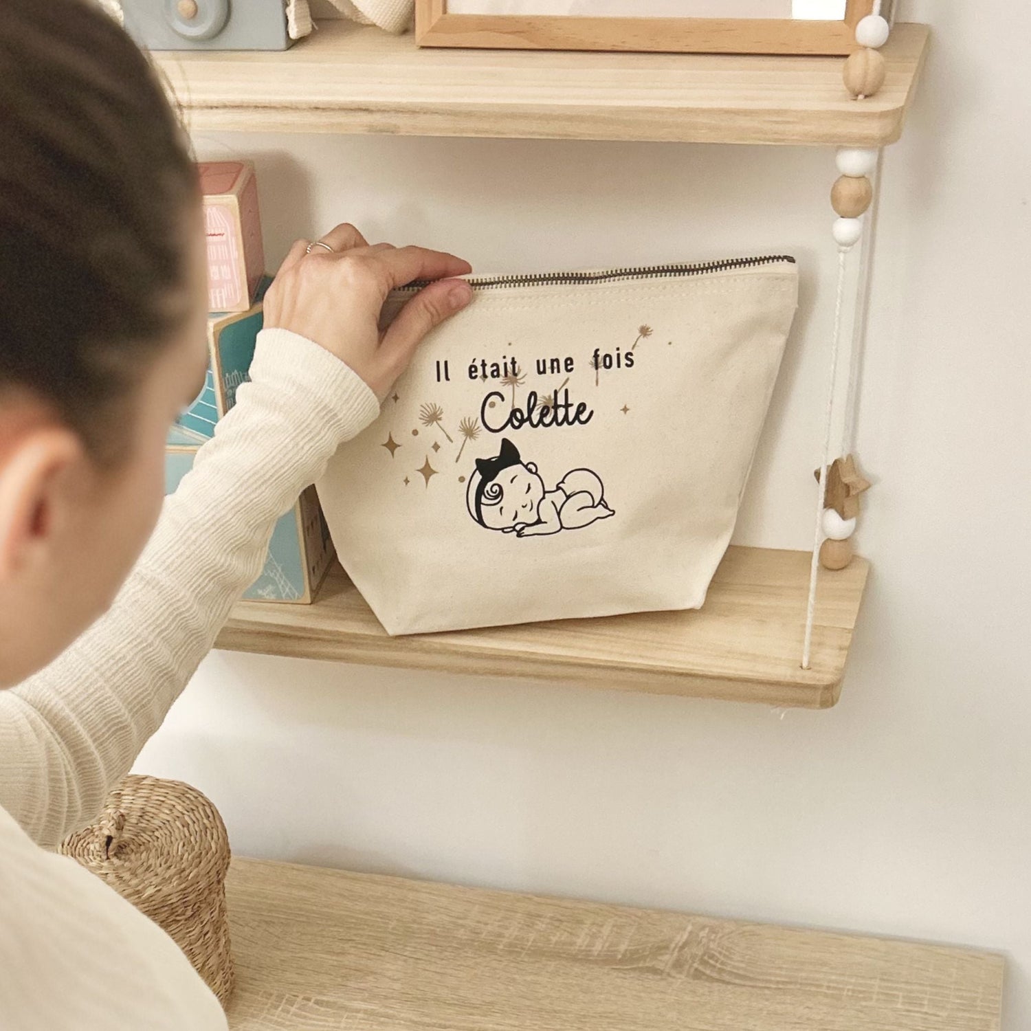 Elodie présente une création Petit Polisson personnalisée avec le prénom de l'enfant appliqué sur une trousse de toilette, dans une chambre bébé bohème.