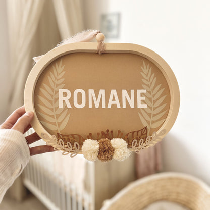 Idée cadeau de naissance personnalisée avec cadre ovale en bois et pompons naturels, ambiance bohème douce.