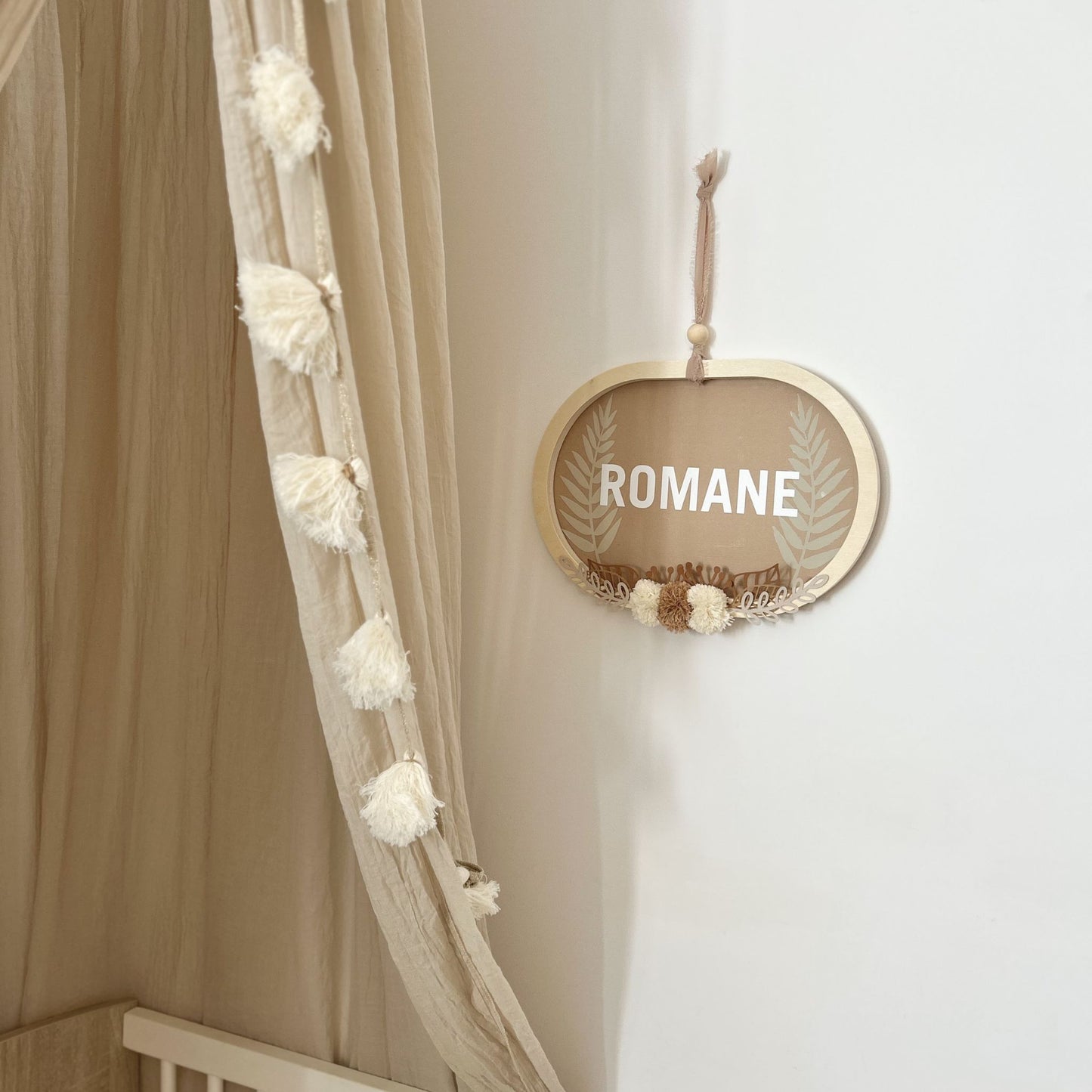 Cadre ovale personnalisé avec le prénom accroché au mur dans une chambre bébé bohème avec ciel de lit.
