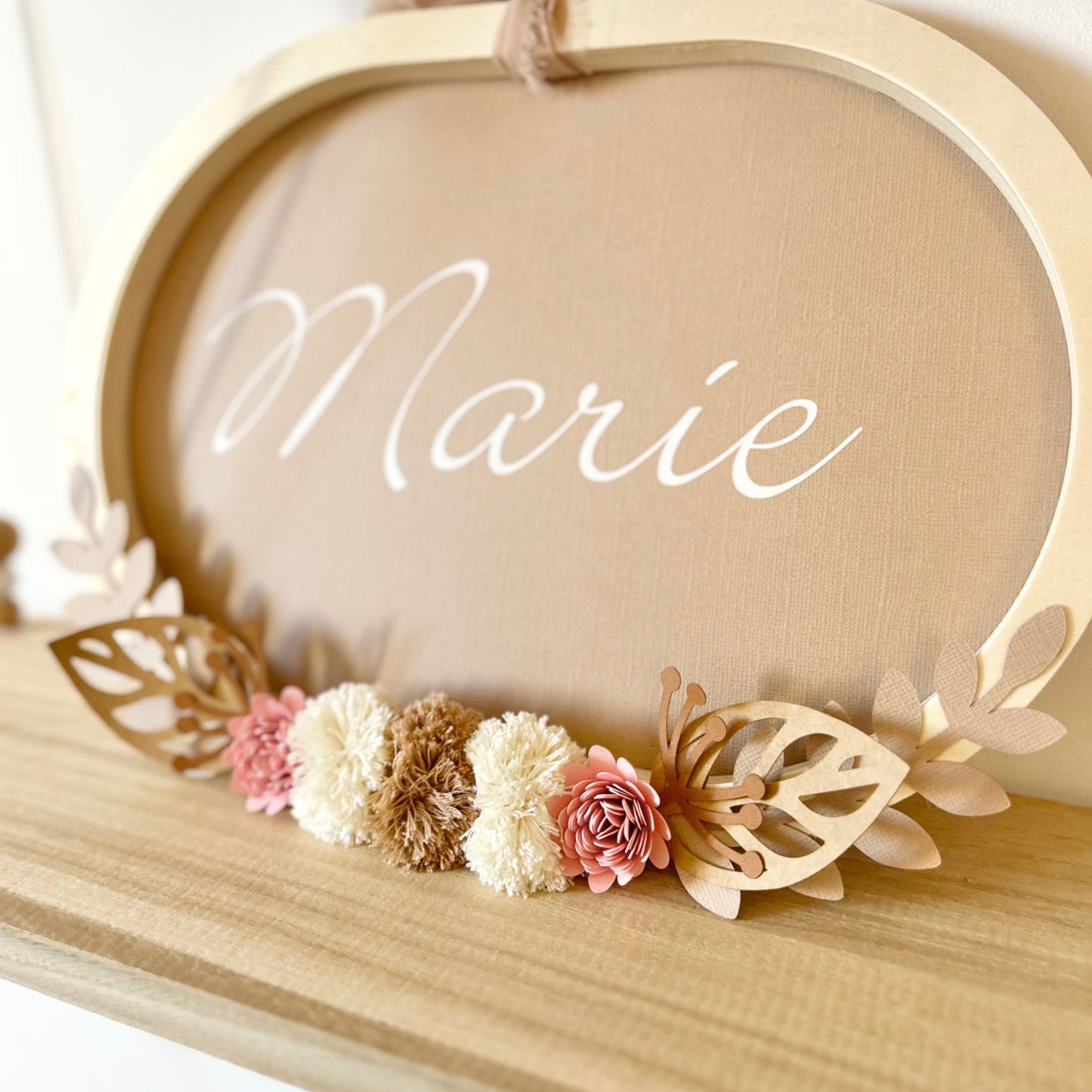 Détail des pompons en laine de coton Oeko-Tex et fleurs artisanales sur cadre prénom Petit Polisson pour décoration chambre bébé tons naturels.