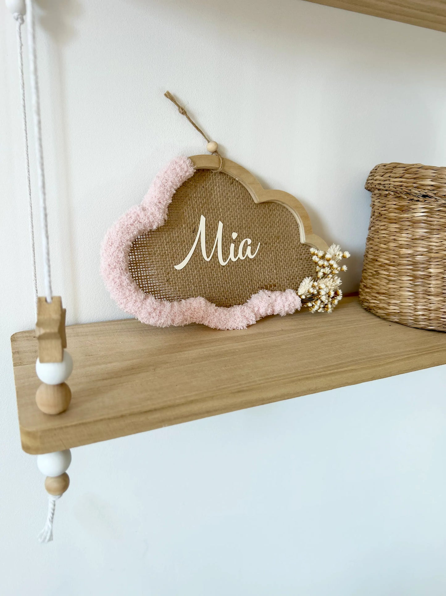 Détail du cadre nuage en bois avec sa laine rose poudré et ses fleurs séchées, posé sur une étagère, parfait pour une ambiance tendre et chaleureuse