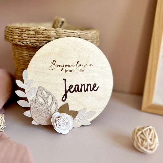 Pancarte ronde en bois gravée, personnalisée avec le prénom de bébé et décorée de fleurs en tons naturels et raffinés.