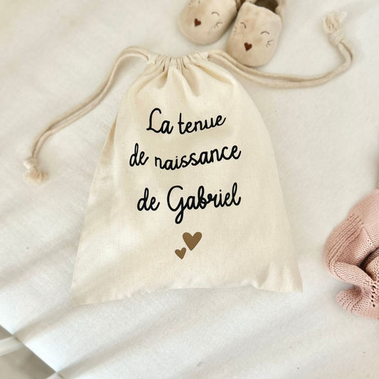 Sac en coton personnalisé avec le prénom  de bébé pour préparer et ranger la tenue de naissance de l’enfant.